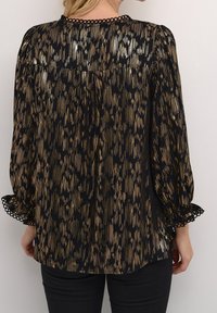 Blouse noire avec des rayures verticales dorées, manches longues bouffantes et poignets à volants. Le dos présente une texture lisse avec un détail d'ourlet subtil.