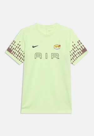 T-shirt de sport Nike vert clair avec le texte "AIR", petit logo swoosh, emblème hexagonal sur la poitrine et motifs bruns à points sur les manches.