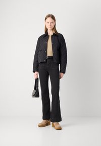 Jachetă neagră matlasată, ușoară, cu design scurt; top bej dedesubt, blugi negri evazați; mules cu toc bej; geantă mică neagră.