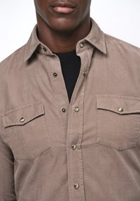 Lichtbruine corduroy blouse met een button-down kraag, twee borstzakken en drukknoopsluiting. De stof heeft een zachte textuur.