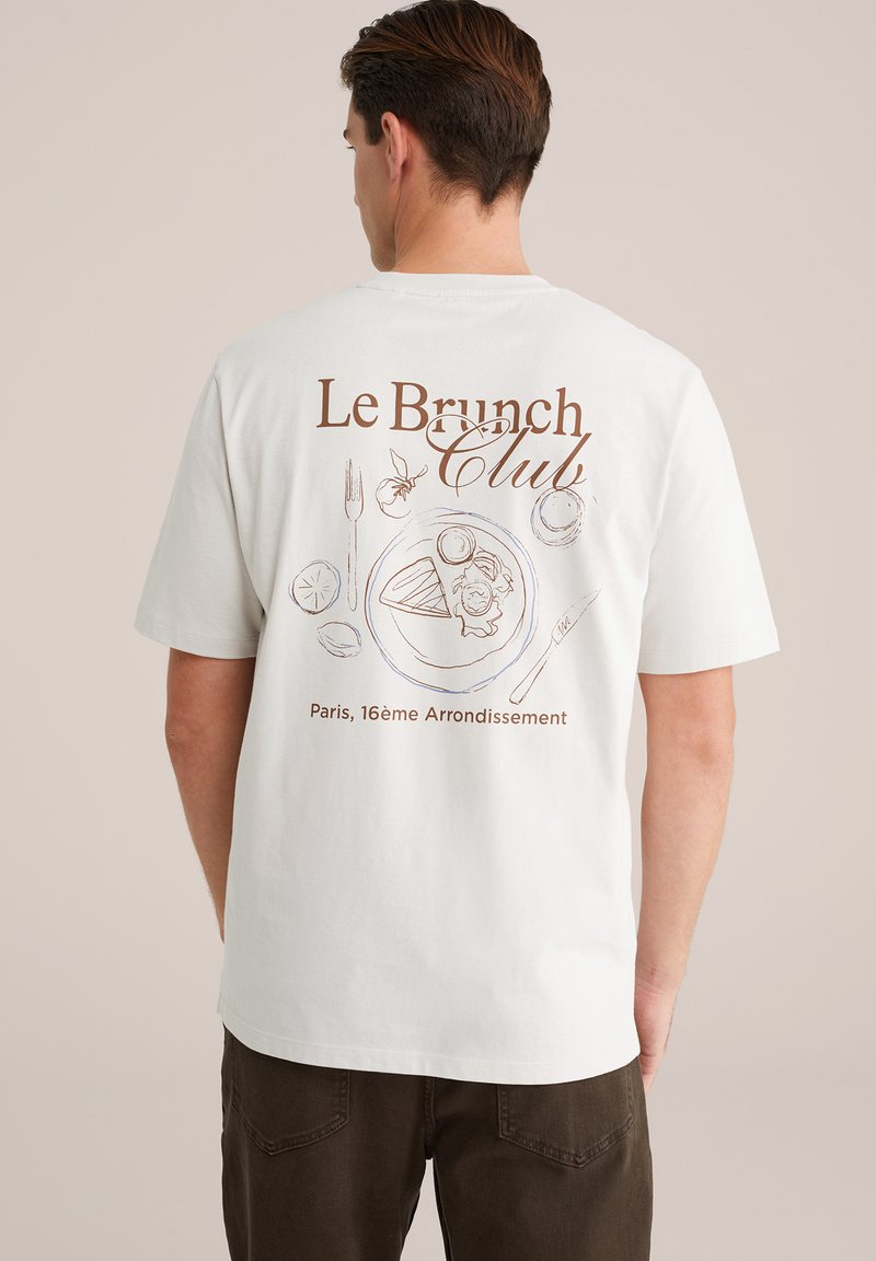 Balta kokvilnas t-kreklu ar brūnu grafiku uz aizmugures, kurā attēlota šķīvis ar ēdienu, galda piederumi un teksts "Le Brunch Club". Vienkāršs, ikdienišķs dizains.