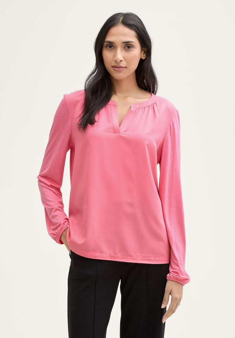 Blusa de manga larga rosa con escote en forma de pico, detalles fruncidos en los hombros y puños elásticos; tejido suave y ligero.