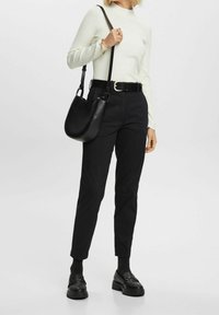 Maglietta bianca a costine a maniche lunghe, pantaloni neri a vita alta, borsa a spalla nera e scarpe nere con plateau, creando un look monocromatico.