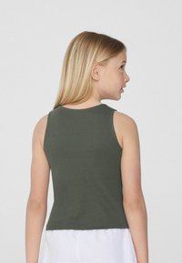 Prążkowany top na ramiączkach w oliwkowym kolorze, z okrągłym dekoltem i bezrękawowym fasonem. Tkanina wydaje się miękka, o dopasowanej sylwetce, krojony do talii.