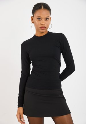 Top nero a maniche lunghe con un design aderente, realizzato in un tessuto liscio. Abbinato a una minigonna nera, creando un aspetto slanciato.