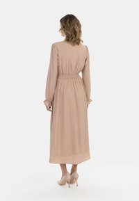 Pitkä, persikankirjava mekko, jossa on istuva vyötärö, puffihihat ja röyhelömäiset hihansuut; sisältää hienovaraisen kuosin, ulottuu polven alapuolelle ja on yhdistetty nude-sandaaleihin.