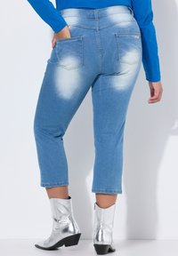 Jeans de mezclilla cortos en un azul claro con un diseño ligeramente deslavado, bolsillos traseros y un detalle de cremallera plateada brillante. Combinados con botas de tobillo plateadas.