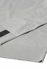 Grauer gestrickter Pullover mit gerippter Textur, der einen schwarzen Streifen an der Manschette und ein kleines gesticktes Logodetail am Ärmel aufweist.