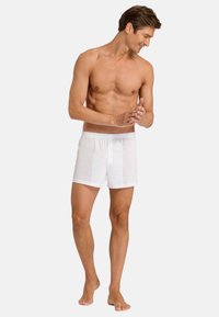 Valkoiset puuvillaiset bokserit, joissa on joustava vyötärö. Kangas on kevyttä ja hieman läpikuultavaa, ja niissä on rento istuvuus sekä sivuhalkiot.