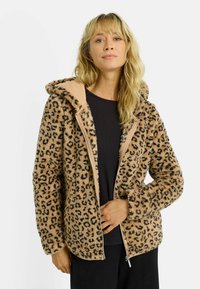 Veste en fausse fourrure camel à imprimé léopard, fermeture éclair devant et capuche. Manches avec poignets côtelés et doublure intérieure contrastée. Texture douce sur toute la surface.