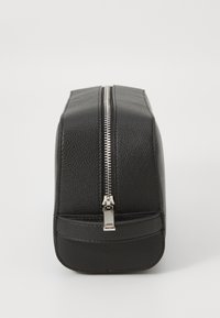 Trousse de toilette en cuir noir avec une finition texturée, de forme rectangulaire et des détails en zip argenté sur le dessus. Surface inférieure lisse.