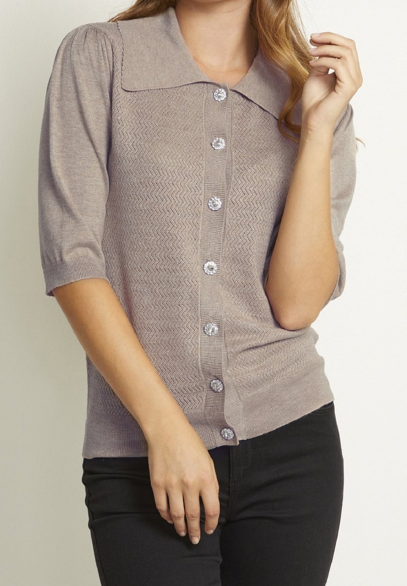 Cardigan lavorato a maglia grigio chiaro con un ampio colletto, maniche a sbuffo corte e bottoni decorativi con un motivo a zigzag.