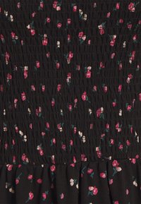 Mustassa kankaassa on teksturoitu, smokkikuvio, jossa on kukkakuosi vaaleanpunaisena, valkoisena ja tealina. Alaosa on röyhelöity.