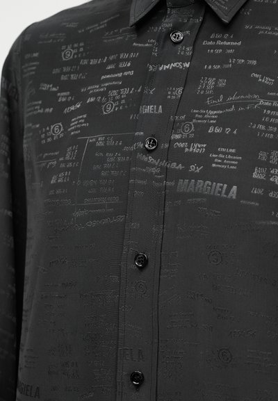 Μαύρο πουκάμισο με υφή από τυπωμένο κείμενο και σύμβολα. Διαθέτει εμπρός μέρος με κουμπιά και κλασικό γιακά.