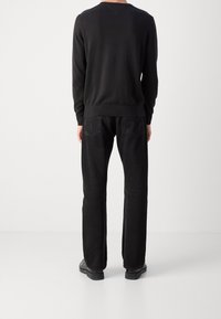 Felpa nera con polsini e orlo a costine, abbinata a jeans neri con tasche posteriori. L'outfit include calzature nere.