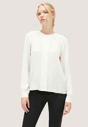Witte blouse met lange mouwen en een ronde halslijn, voorzien van subtiele verticale plooien en licht verzamelde manchetten, gecombineerd met zwarte broek.