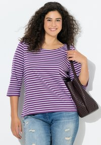 Lila-weiß gestreiftes Langarmshirt mit rundem Ausschnitt, weichem Stoff, kombiniert mit einer braunen, geflochtenen Umhängetasche und hellblauen, verwaschenen Jeans.