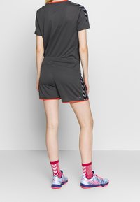 Top atlético de color gris oscuro y pantalones cortos con ribete rojo, con un patrón de chevron en los lados. Se lleva con zapatillas coloridas y calcetines estampados.