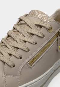 Μπεζ αθλητικό παπούτσι με υφή στο πάνω μέρος, χρυσές λεπτομέρειες και κορδόνια σε κρεμ απόχρωση. Διαθέτει διακοσμητικό πλευρικό φερμουάρ και ραμμένες λεπτομέρειες.
