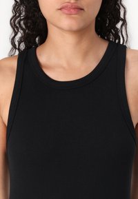 Zwarte geribbelde tanktop met een ronde halslijn; aansluitend ontwerp, gemaakt van een gladde stof met een subtiele textuur, minimale naden aan de randen.