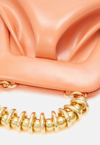 Sac à main en cuir pêche avec un design plissé, doté d'une anse chaîne dorée composée d’anneaux et de sphères entrelacés. Texture lisse.