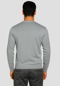 Maglione grigio a maniche lunghe, trama lavorata a maglia, scollatura rotonda e polsini a coste. Abbinato a pantaloni grigio scuro con due tasche posteriori.