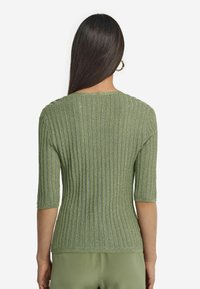 Stickad tröja i ljusgrön med ribbat mönster, som har rund halsringning och ärmar i armbågs längd. Bakre vy visar passformen och designen.