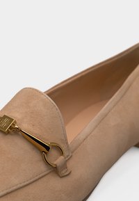 Μπέζ μοκασίνι από σουέντ με χρυσή μεταλλική λεπτομέρεια horsebit στο επάνω μέρος, διαθέτει χαμηλό τακούνι και λείο εσωτερικό επένδυση.