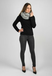 Un pull noir à manches longues associé à un jean foncé et des chaussures à talons hauts noires. Porté avec une écharpe en tricot gris chunky.