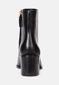Czarny skórzany botek za kostkę z zaokrąglonym noskiem i średniej wysokości obcasem w formie słupka. Posiada zamek błyskawiczny oraz wytłoczone logo na pięcie.