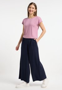 T-shirt rosa aderente a maniche corte abbinato a pantaloni larghi blu navy. I pantaloni hanno tasche laterali, indossati con sneakers bianche.