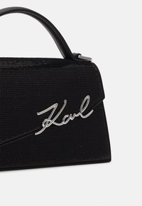 Sac à main noir texturé avec une poignée incurvée et un détail signature argenté "Karl" sur le rabat avant.