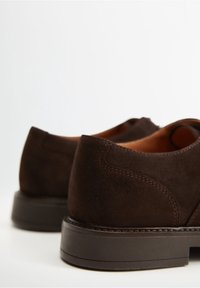 Chaussures en daim marron avec une texture lisse, une forme arrondie et des détails de coutures contrastantes. Semelle épaisse marron avec une légère élévation du talon.