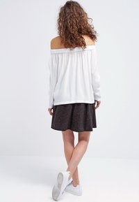 Top blanco de manga larga y sin hombros combinado con una falda gris oscuro. La modelo lleva zapatillas blancas. Tejido suave, diseño de corte relajado.