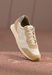 Beige og hvid sneaker lavet af ruskind og lædermaterialer, med en stjerne-logo og snørebånd. Struktureret sål med gummigreb.
