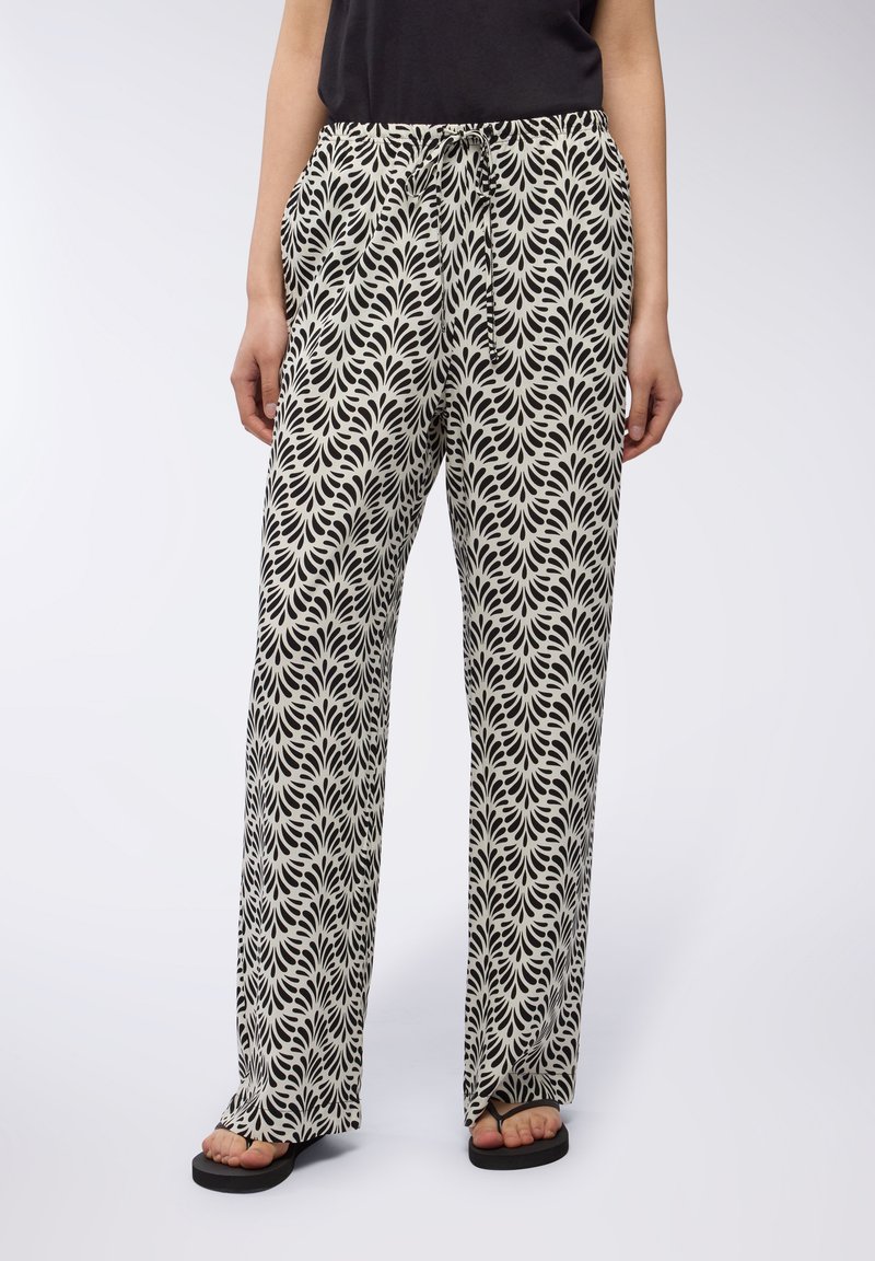 Pantaloni a gamba larga in bianco e nero con motivo, vita con cordoncino, tessuto leggero e tasche laterali, abbinati a ciabatte nere.