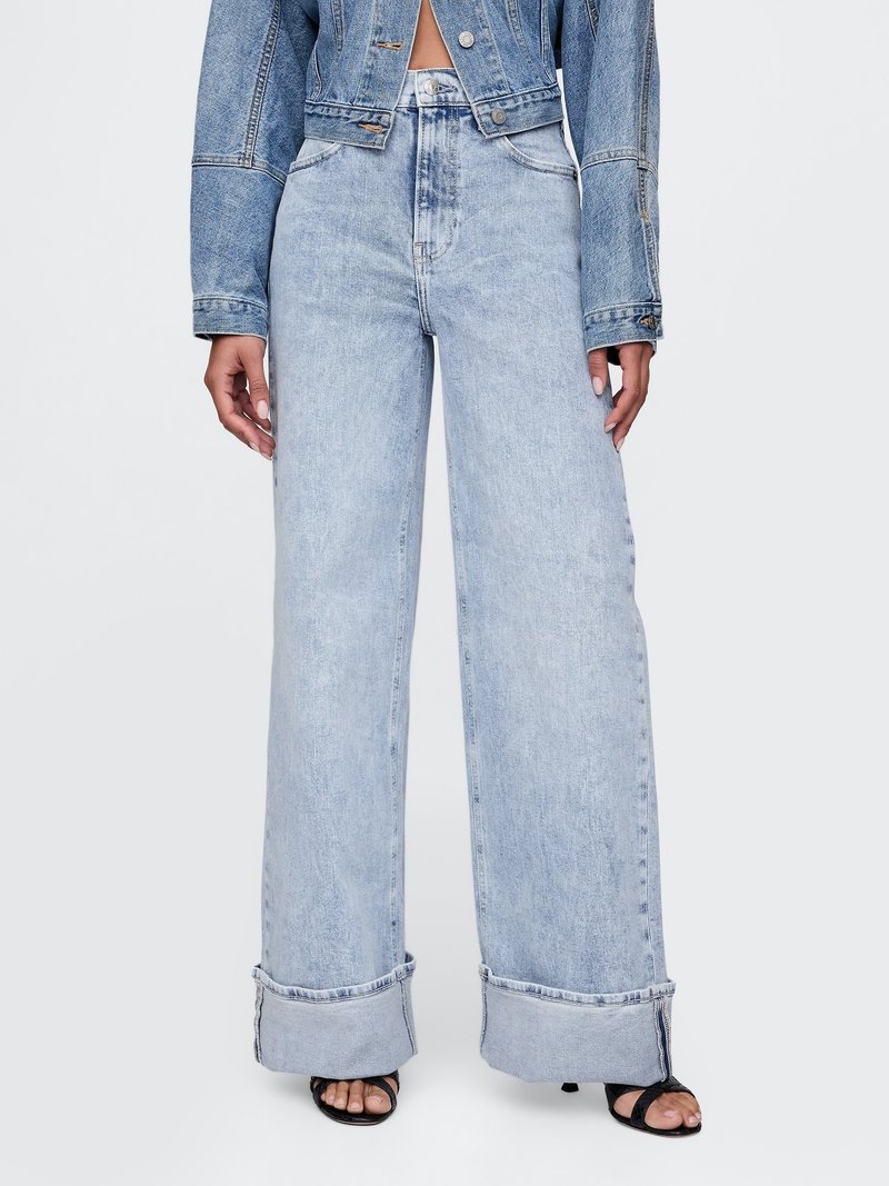 Jasnoniebieskie dżinsy o szerokich nogawkach mają wysoki stan, wyblakły denim i podwinięte mankiety. Materiał ma gładką fakturę z minimalnymi detalami przeszyć.