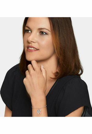 Bracciale d'argento con charm a foglia, caratterizzato da una catena delicata e accenti testurizzati, indossato su un polso. Camicia scura sul sfondo.