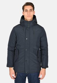 Giacca puffer blu navy con cappuccio, chiusura a zip e bottoni a pressione. Presenta due tasche laterali e una texture liscia e resistente all'acqua.