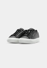 Sorte sneakers laget av glatt tekstil med rund tå, tykk hvit gummisåle, tonede lisser og logo-detalj på siden.