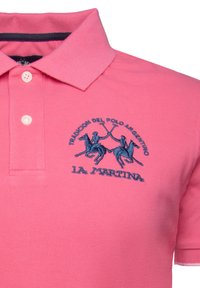 Ljusrosa polo t-shirt med en texturerad yta, med en marinblå broderad logotyp av ryttare och texten "LA MARTINA". Treknappsknäppning vid kragen.