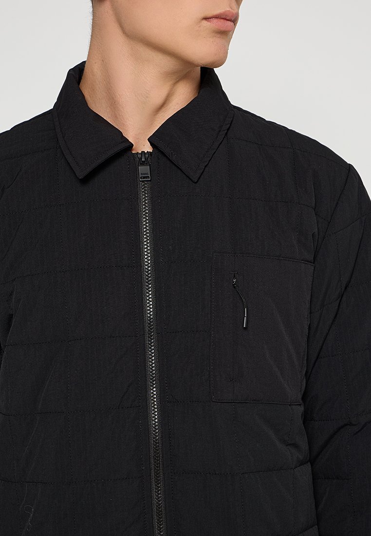 Svart vadderad jacka med ståkrage, framsidan med dragkedja och en liten dragkedjeficka på bröstet. Tillverkad av texturerat tyg.