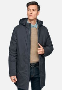 Giacca isolante grigio scuro con cappuccio, dotata di chiusura a zip, tasche laterali e un maglione beige testurizzato sotto.