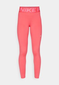 Korálově růžové legíny Nike Pro s vysokým pasem a širokým elastickým pasem, na kterém je text "NIKE PRO" a malý bílý znak Nike na levém stehně.