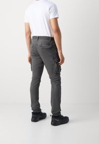 Szare spodnie cargo z bocznymi kieszeniami, fason slim fit i fakturowany materiał. Połączone z gładką białą koszulką i czarnym obuwiem.