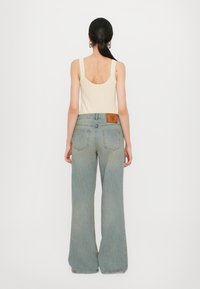 Top a costine crema abbinato a jeans a gamba larga blu chiaro con una toppa in pelle nella parte posteriore della vita e due tasche posteriori.