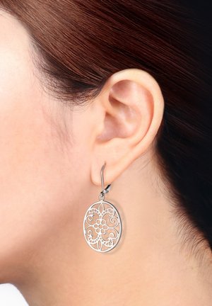 Pendientes de filigrana de plata con forma ovalada, que presentan patrones florales y cierre de gancho, colgando cerca de la oreja.