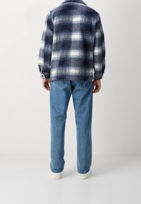 Giacca a quadri blu e bianca con una texture morbida, abbinata a jeans azzurri e sneakers bianche. Cuciture e bottoni visibili sulle maniche.