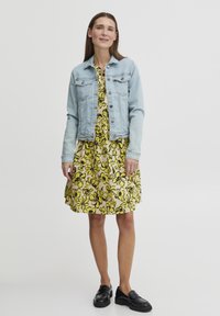 Šviesiai mėlynas džinsinis švarkas ant geltonos gėlių suknelės su juodais akcentais, derinamas su juodais loafers. Lygus audinys, laisvas kirpimas.