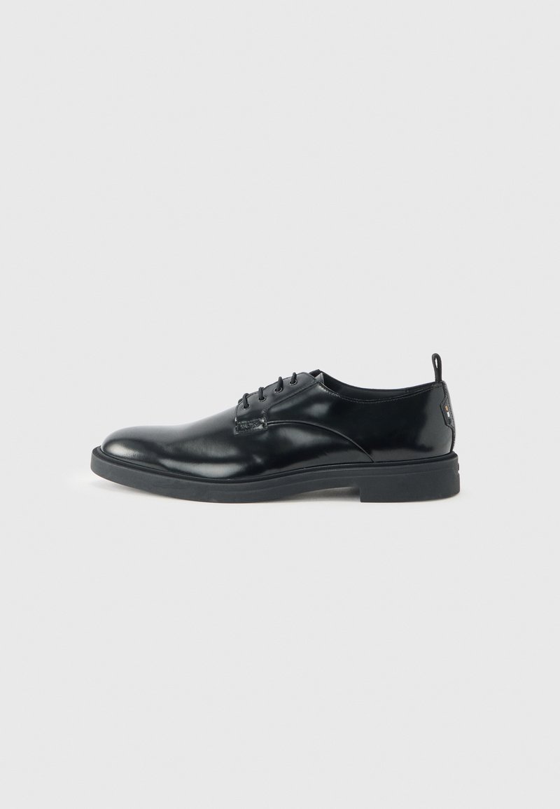 Chaussure habillée pour homme en cuir noir poli avec fermeture à lacets et petit talon, vue de côté sur un fond clair uni.